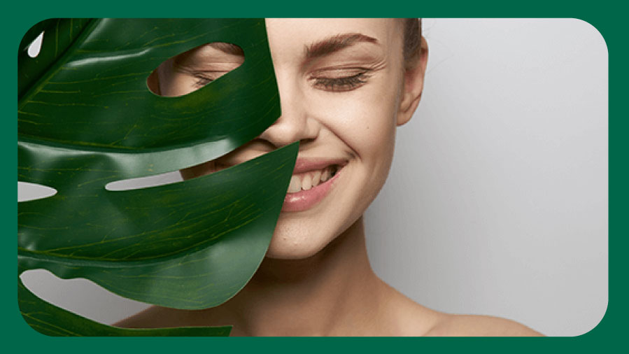 Smiling woman with half her face covered by a leaf, highlighting natural beauty and skincare Smiling woman with half her face covered by a leaf, highlighting natural beauty and skincare